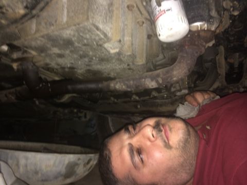 2011 Ford Elite - This photo shows the underside of a vehicle, focusing on the exhaust system and oil filter, with a mechanic attending to it.