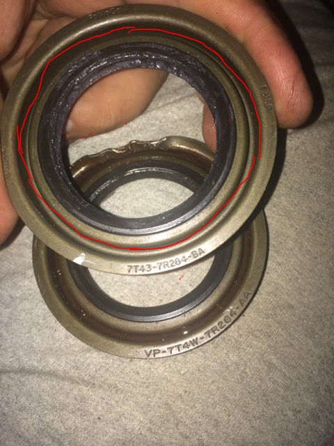 2011 Ford Elite - Close-up of two metal seals, one showing damage and red markings, the other displaying part numbers.