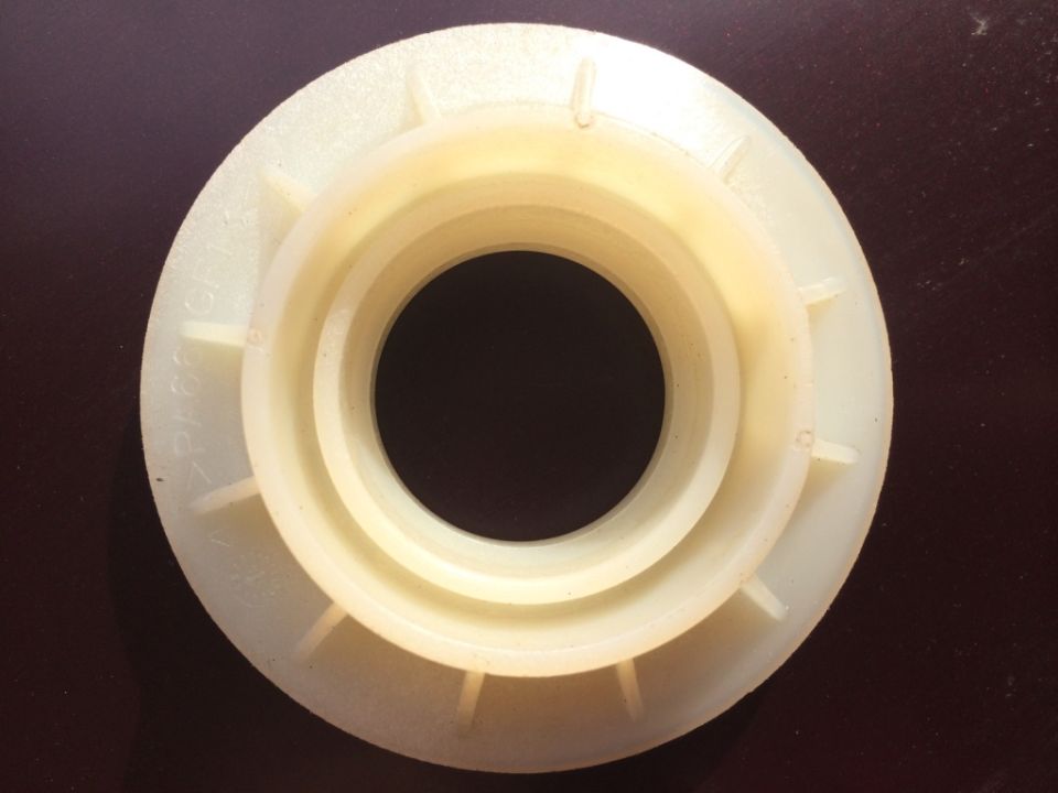 Cream-colored plastic part with concentric rings and radial fins. Text visible