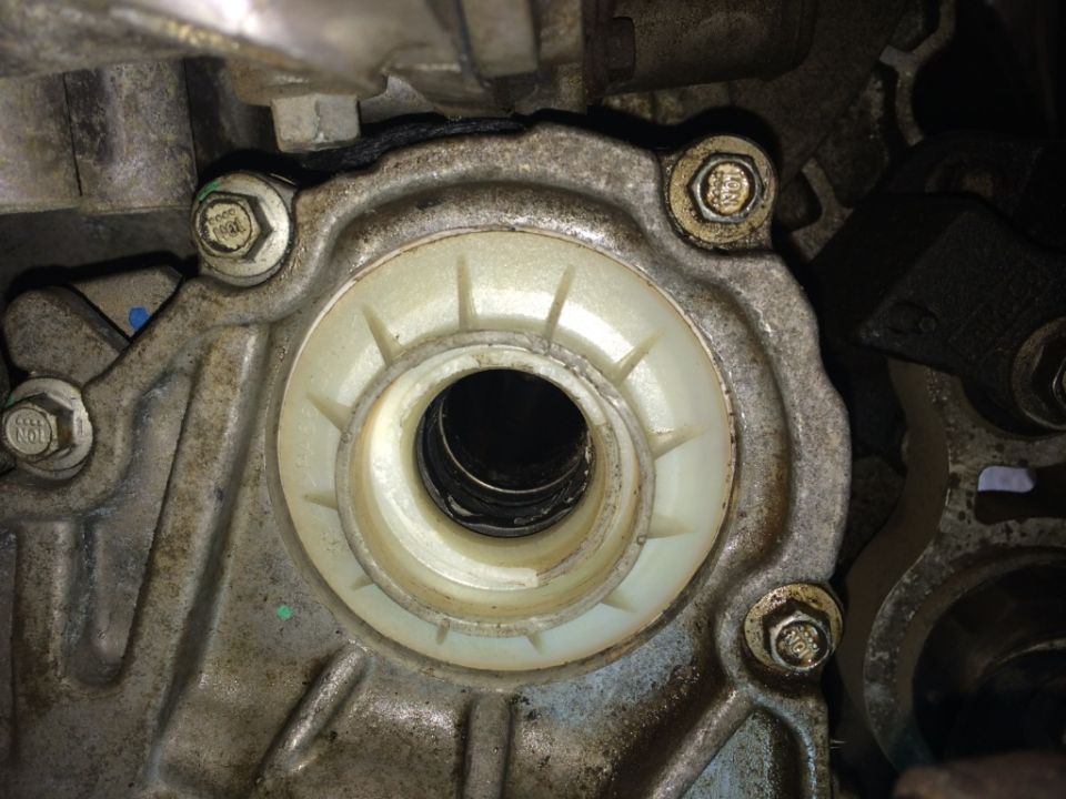 Close-up of a metal engine component with a white plastic seal and several bolts