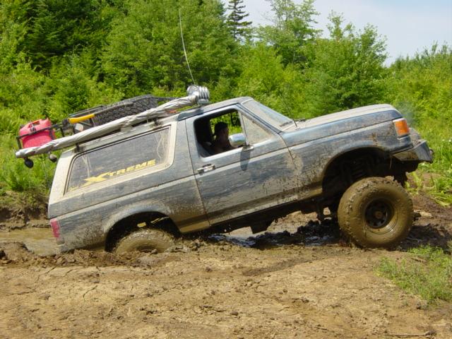 1989 Ford Bronco stuck in mud, side view, with roof rack and spare tire