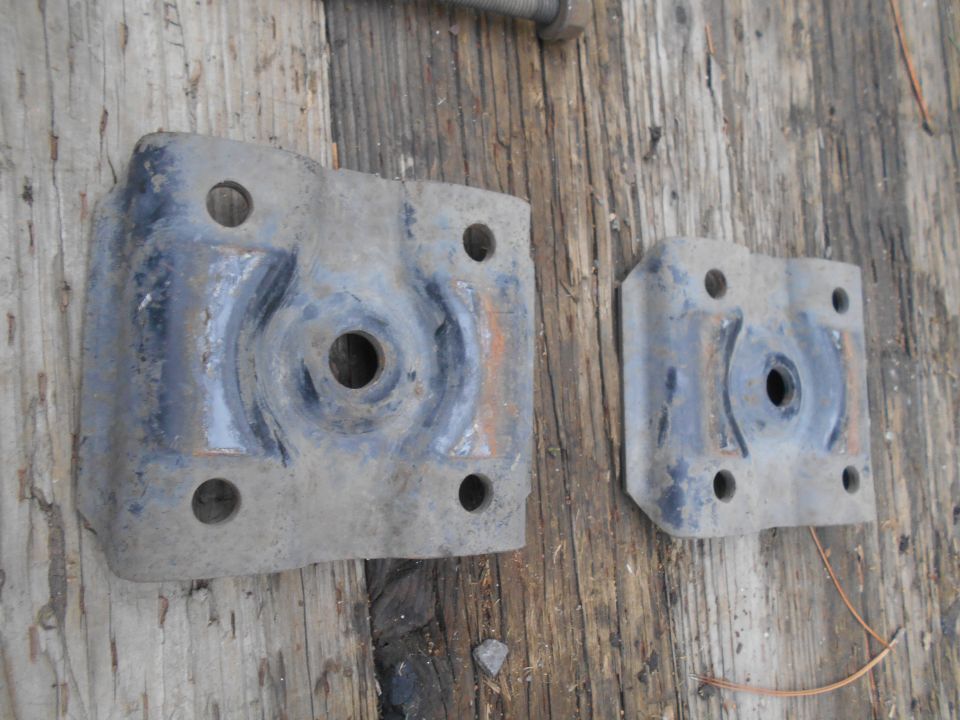 Two dusty, gray metal brackets with four bolt holes each, lying on a wooden surface