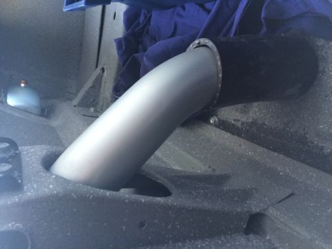 Polished metal exhaust or intake downpipe under vehicle with blue tarp