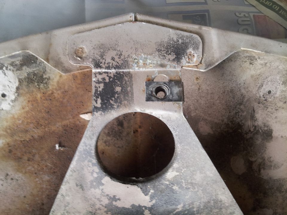 Close-up of a metal vehicle part with a circular opening and a nut clip