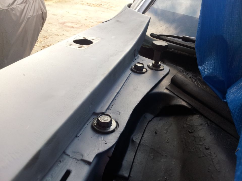 Close-up of car cowl area showing bolts and a blue tarp