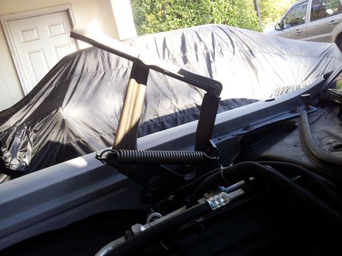 1976 Ford Ranchero - Hood hinge mechanism shown in detail, with a tarp-covered vehicle behind it.