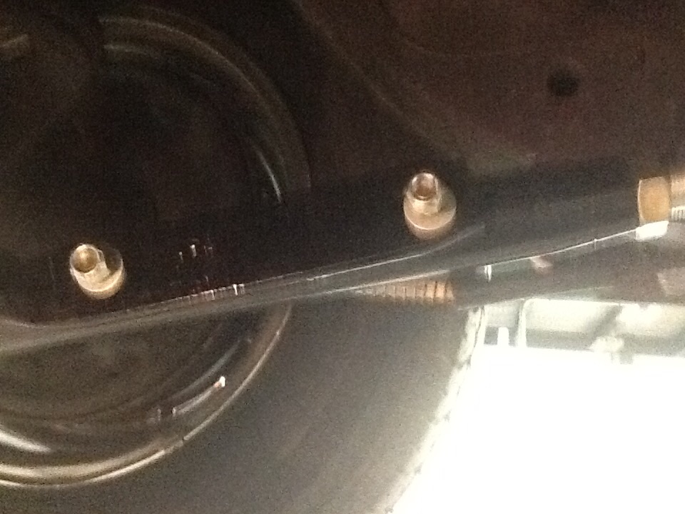 Dim underside detail of a car showing two brass studs on a black panel above a whitewall tire