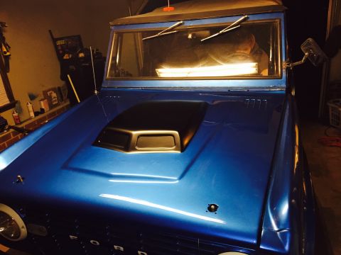 1974 Ford Bronco - 1974 Ford Bronco in garage, showing front end with aftermarket hood scoop and blue paint.