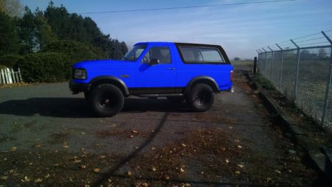 1994 Ford Bronco - A bright blue two-door full-size Ford Bronco SUV shown in side profile with a black hardtop, black rocker panels and fender flares, lifted…