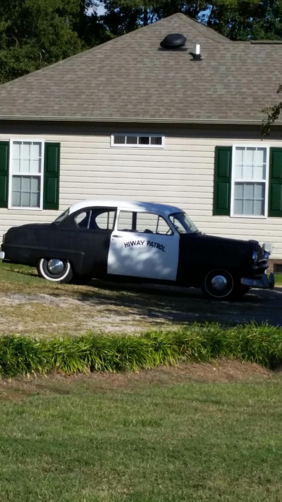 1953 Plymouth Belvedere Highway Patrol car, black and white, parked in front of a house.
