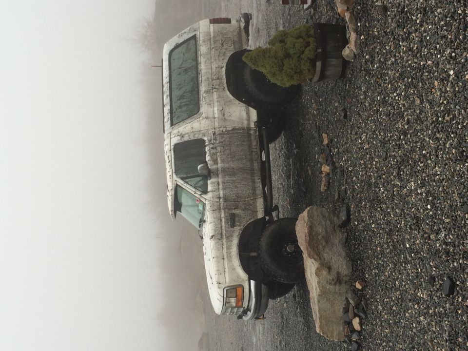 Dirty white Ford Bronco parked on gravel in fog.