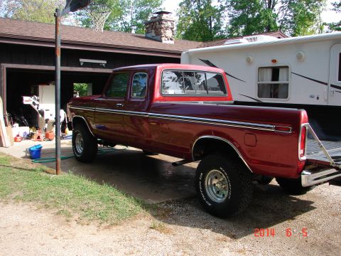 1979 Ford F-150 - A red 1979 Ford F-150 pickup truck is parked in a driveway next to a white RV. The truck has a crew cab and is lifted with large off-road t…
