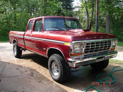 1979 Ford F-150 - A red 1979 Ford F-150 pickup truck is parked on a concrete driveway with a wooded area in the background. The truck has a crew cab, chrome…