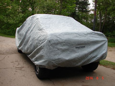 1979 Ford F-150 - A light gray car cover obscures a vehicle, revealing only the tires and a portion of the rear fender. The cover has the Rust-Oleum logo pri…