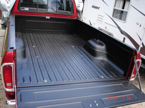1979 Ford F-150 - The open tailgate and bed of a red Ford pickup truck are shown, featuring a black spray-in bed liner. A white RV is parked behind the truck.