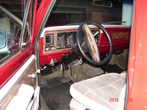 1979 Ford F-150 - Interior view of a red 1979 Ford F-150 pickup truck, showing the dashboard with wood grain trim, steering wheel, and driver's seat.