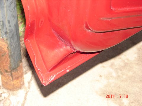 1979 Ford F-150 - Close-up view of the lower corner of a red vehicle door or fender, showing damage and a dent. A rusted metal pole is visible to the left of…