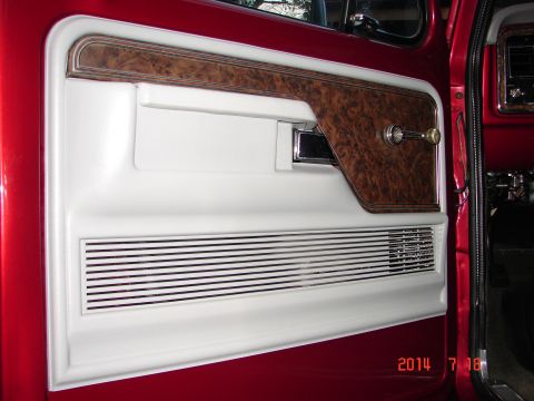 1979 Ford F-150 - The interior door panel of a red 1979 Ford F-150 features a wood grain accent panel with a chrome window crank and a speaker grille with ho…