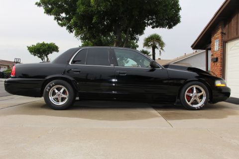 2003 Ford Crown Victoria - Side profile photo of a lowered black Ford Crown Victoria with polished drag wheels in a residential driveway.