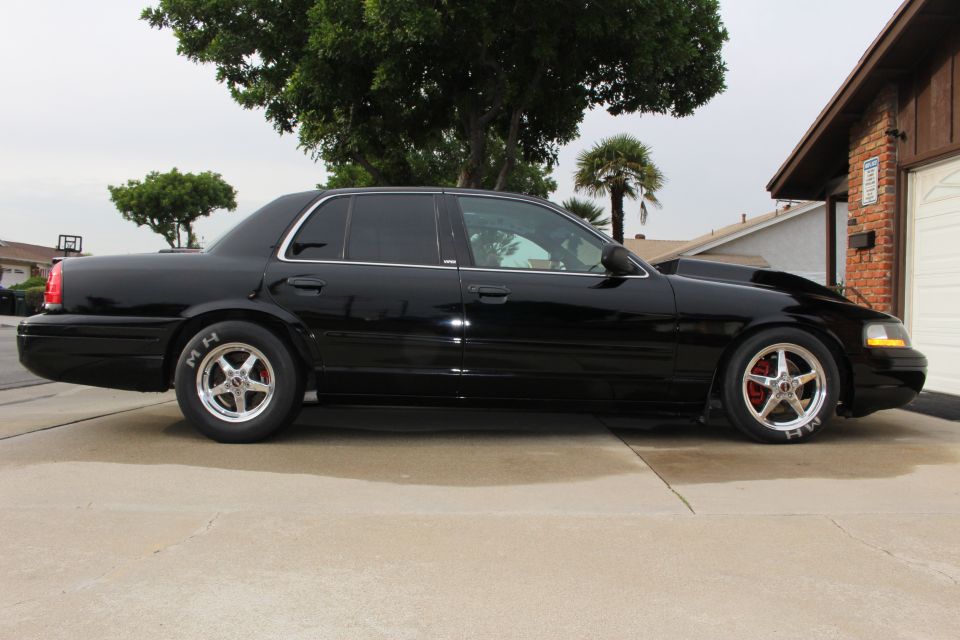 Black Ford Crown Victoria sedan parked in a driveway, side profile view
