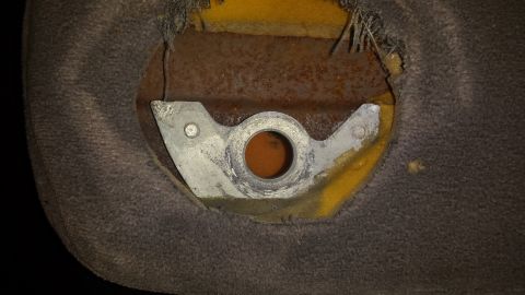 1995 Ford Bronco - A close-up view reveals a metal bracket with a circular opening, attached to the underside of a worn, brown fabric seat with yellow foam pa…