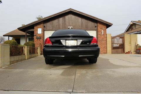 2003 Ford Crown Victoria - Rear view of a black Ford Crown Victoria parked in a driveway facing a brick house.