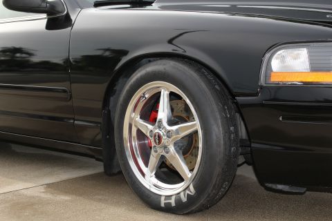 2003 Ford Crown Victoria - Close-up photo of a black Crown Victoria front wheel with polished drag rim, M/H tire, and red caliper.