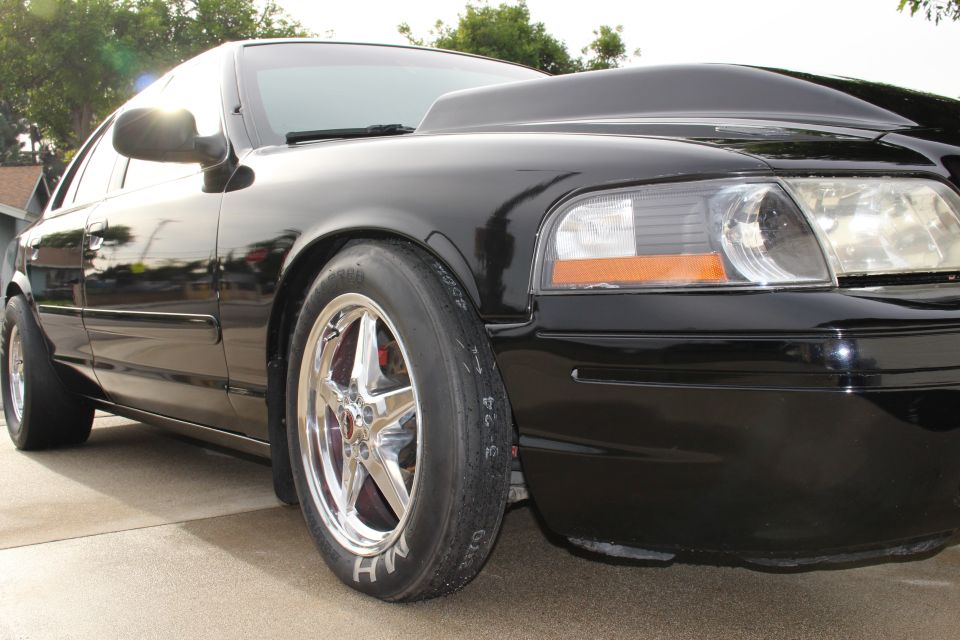 Low front-corner view of black Crown Victoria and front wheel