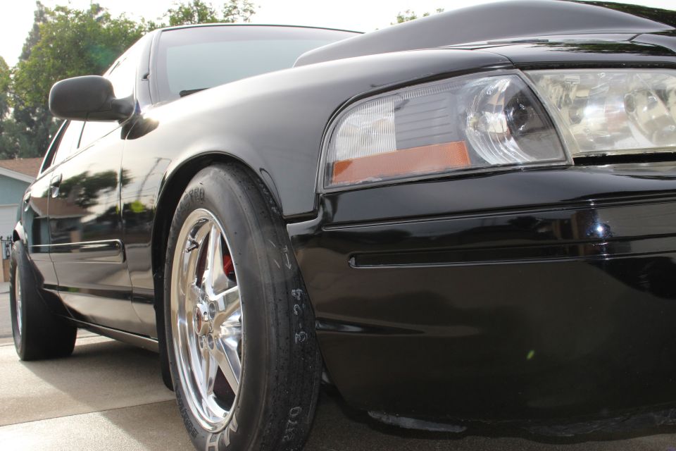 Low front-corner view of black Crown Victoria and headlight