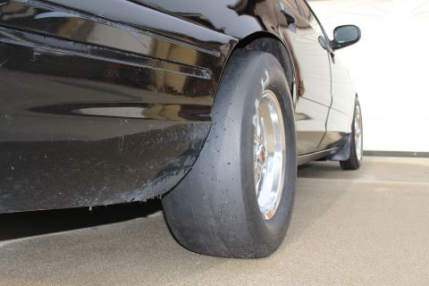 2003 Ford Crown Victoria - Photograph of a black sedan's rear quarter showing a wide drag slick on a polished aluminum wheel, not a technical document.