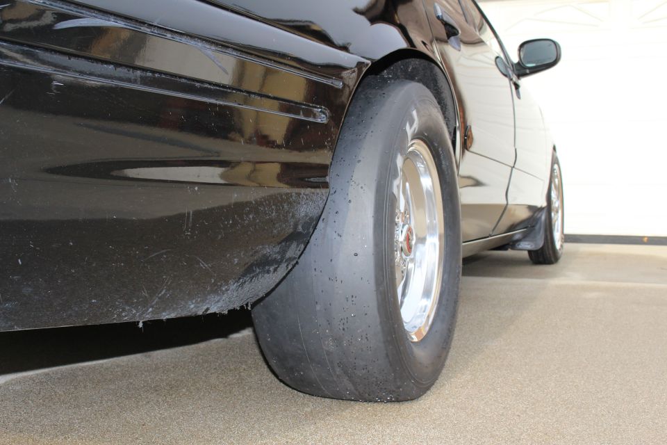 Rear fender and slick drag tire on polished wheel of a black sedan in a garage