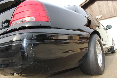 2003 Ford Crown Victoria - Photograph of the rear corner of a black sedan showing the taillight and a rear drag slick, not a technical document.