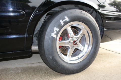 2003 Ford Crown Victoria - Photograph of an M&H drag slick tire on a polished five-spoke wheel of a black car, not a technical document.