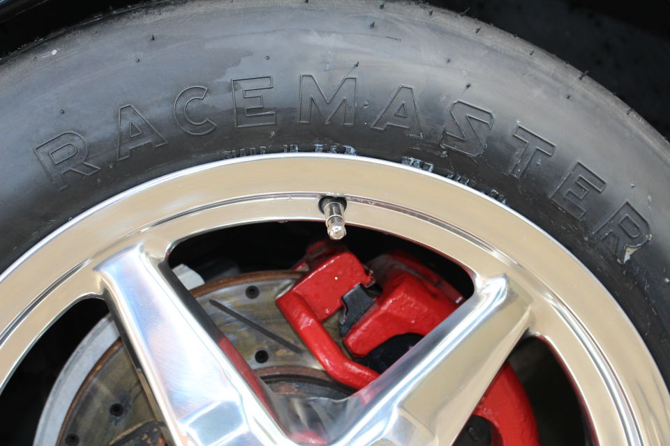 Close-up of a Racemaster tire sidewall, polished wheel spoke, and red brake caliper
