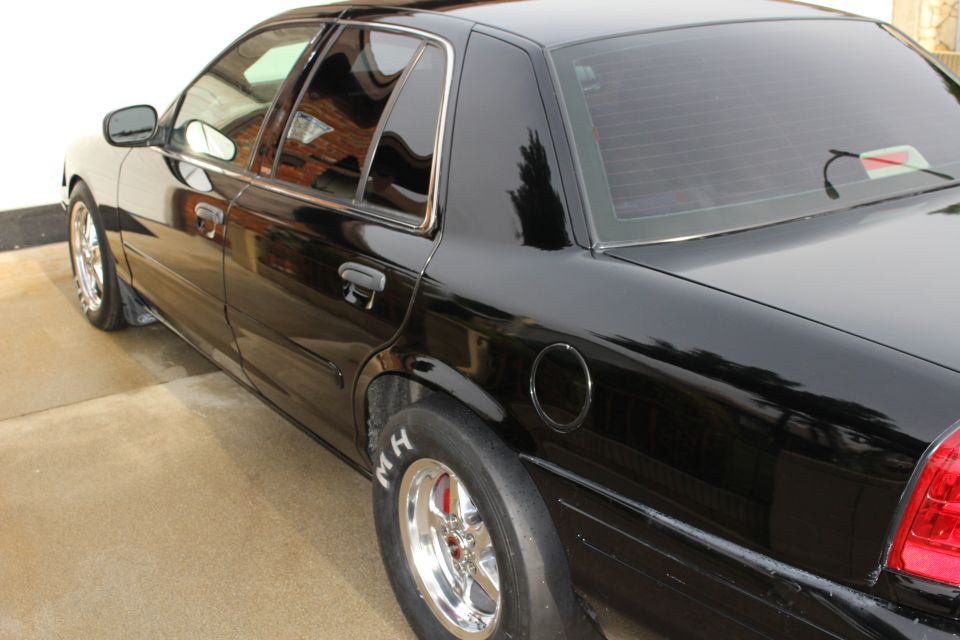 Side and rear view of a black sedan with drag slicks in a driveway