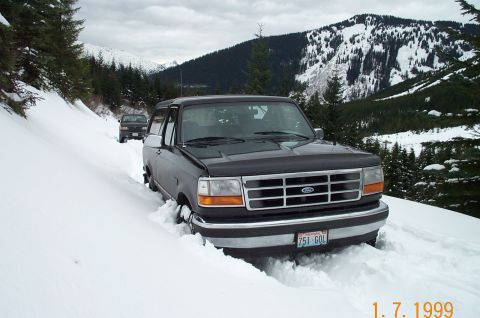 1995 Ford Bronco - Two vehicles navigate a snow-covered mountain pass, with the lead vehicle partially submerged in snow.