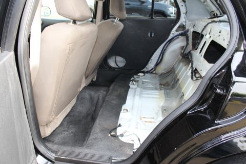 2003 Ford Crown Victoria - Photograph of a black sedan's stripped rear interior showing the bare floor and wheel tub, not a technical document.