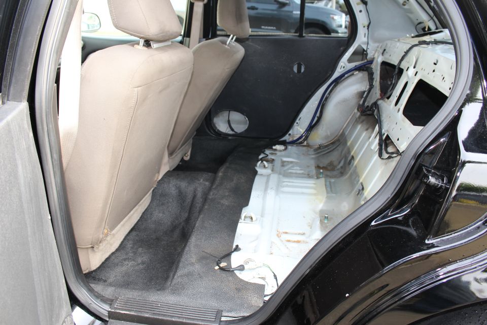 Stripped rear interior of a black sedan showing bare floor and wheel tub