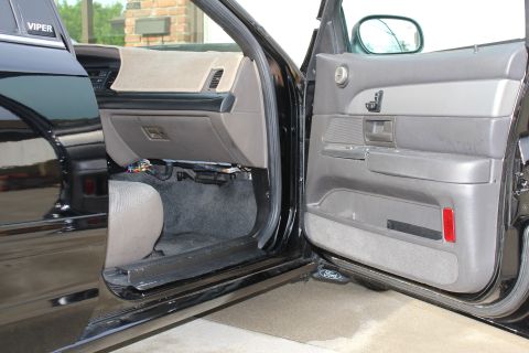 2003 Ford Crown Victoria - open front door of a black sedan showing the gray door panel and dash, with a Ford logo on the door sill plate.