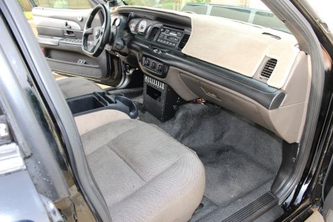 2003 Ford Crown Victoria - dashboard, steering wheel and gray cloth front seats of a black sedan viewed from the open passenger door.