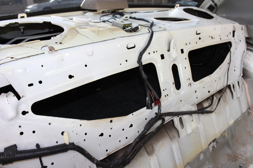 Bare white painted rear bulkhead of a car under glass with wiring harness routed across