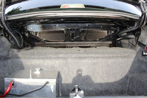 2003 Ford Crown Victoria - rear bulkhead inside a car trunk, showing carpet, a battery box with a red cable and routed wiring.