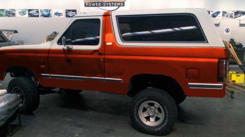 1982 Ford Bronco - This two-tone orange and white SUV is shown from the side, with a white hardtop and chrome trim. The body style suggests a model from the e…