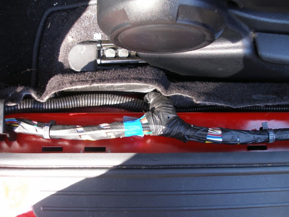 Vehicle wiring harness wrapped in black tape and zip ties, running along a red metal frame.