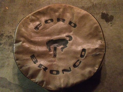 1990 Ford Bronco - A brown leather tire cover with the Ford Bronco logo is shown on a concrete surface. The cover features the word "FORD" in an arc above a s…
