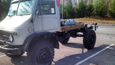 1979 Ford Bronco - A light gray, four-door truck with large off-road tires is parked in a paved lot. The truck bed carries two gray propane tanks secured to a…