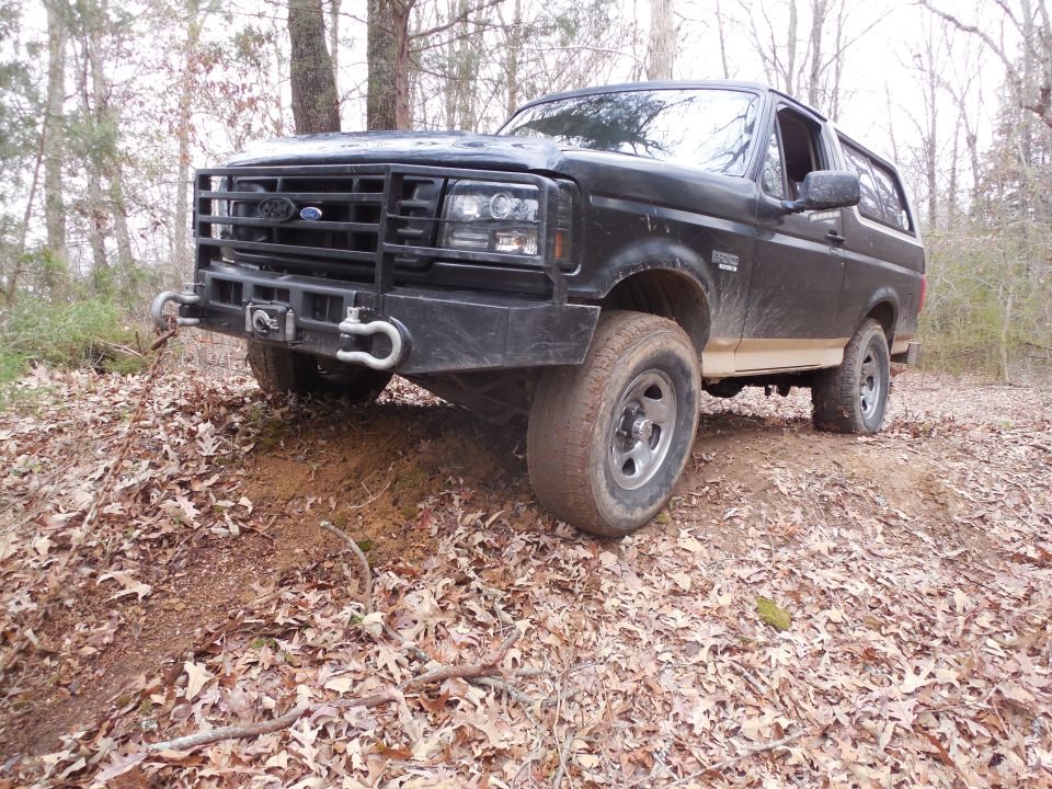 Black Ford Bronco with brush guard and winch bumper climbing a dirt bank in the woods