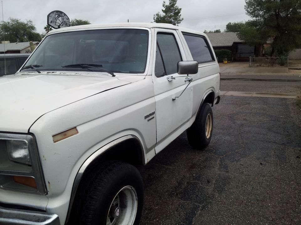 White 1980s Ford Bronco parked on asphalt driveway.