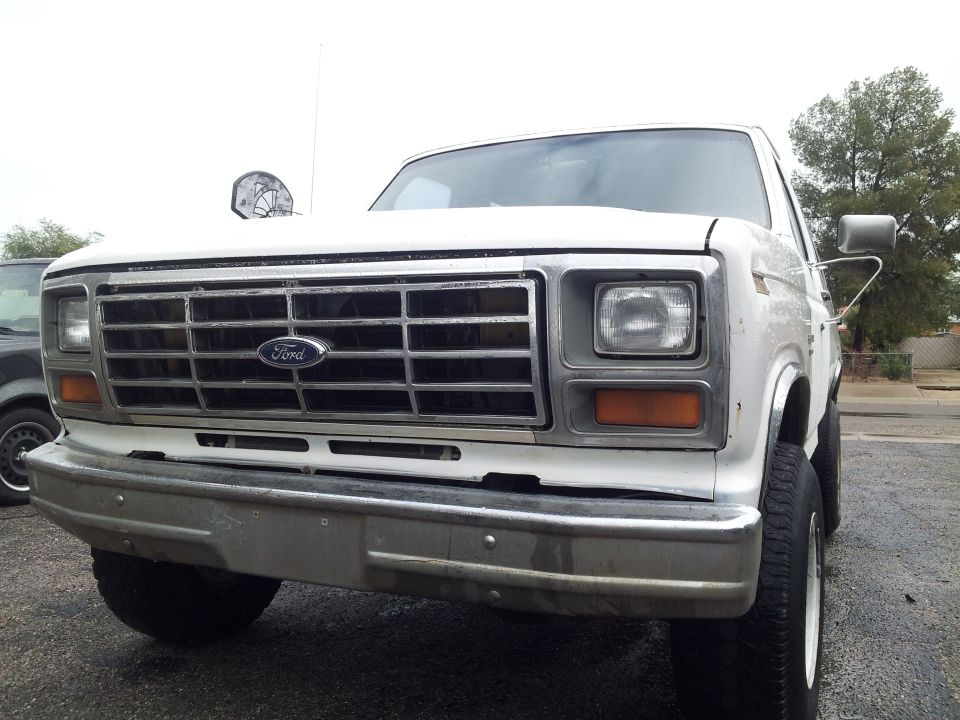 White Ford pickup truck front view, chrome grille, chrome bumper, parked outside.