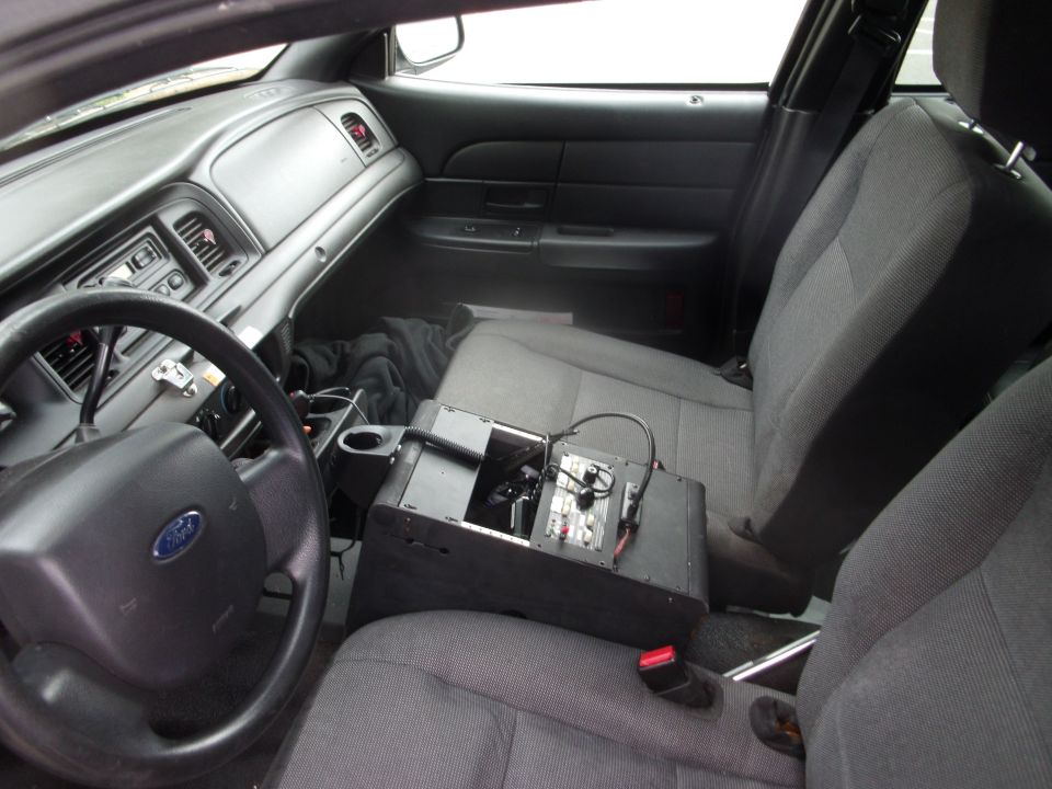 Interior of a Ford Crown Victoria showing dashboard, steering wheel, and center console with electronic device.